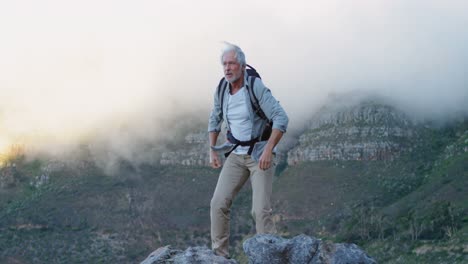 senior man standing with arms up on a rock at countryside 4k