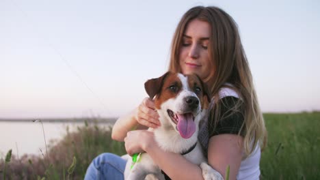 young happy woman and het little dog sitting with flying kite on a glade at sunset