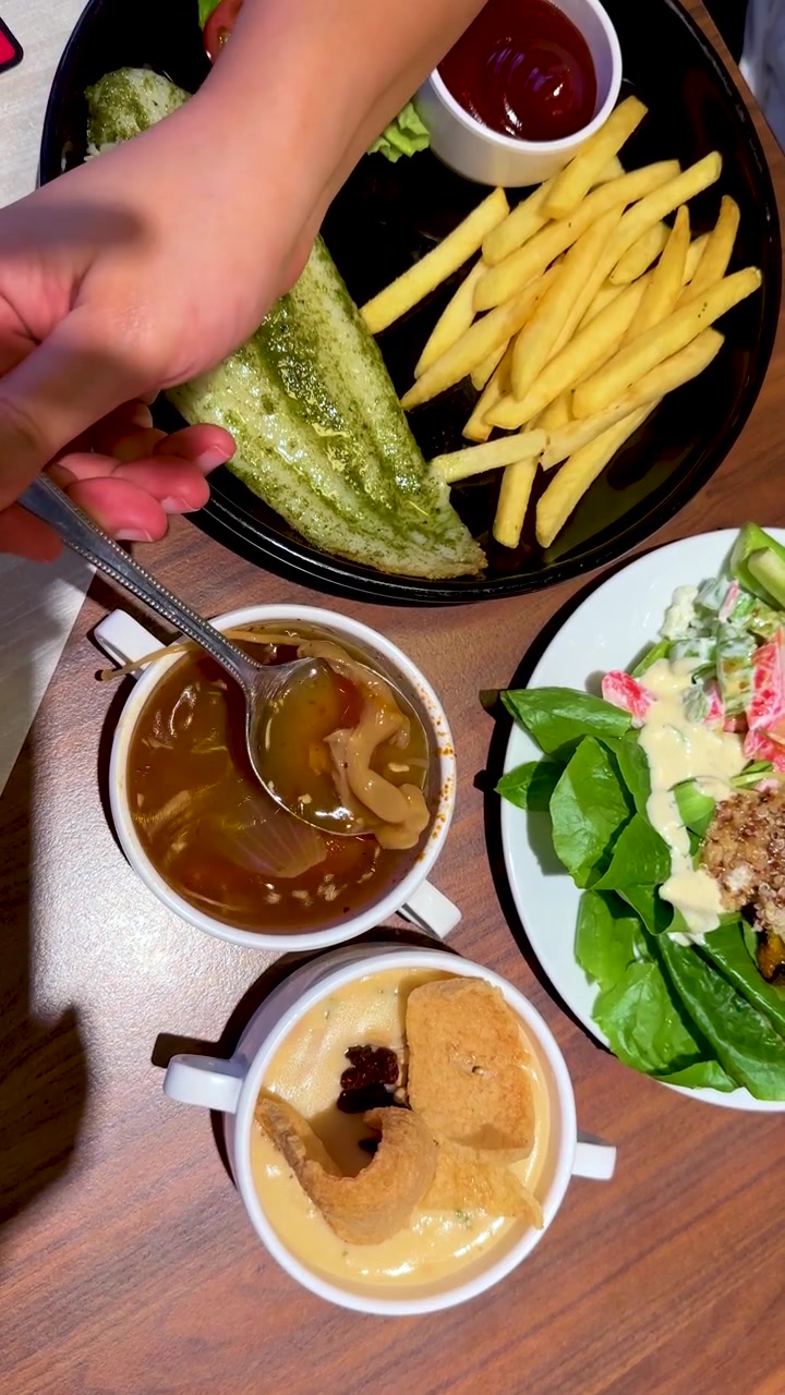 Pemandangan dari atas seseorang mengaduk saus cokelat di samping salad, kentang goreng, dan sup krim