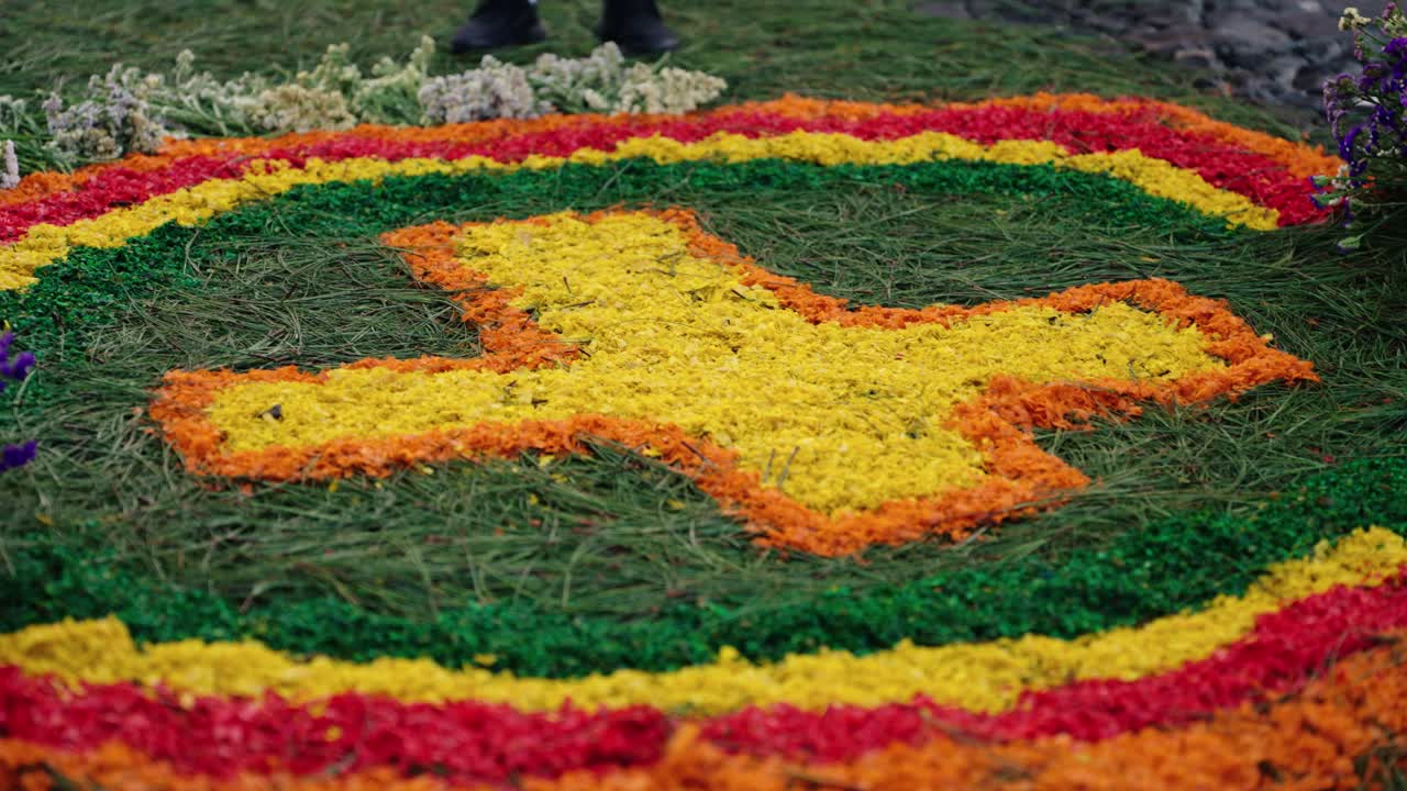 A vibrant sawdust carpet with a yellow cross surrounded by vivid colors during Semana Santa in Antigua Guatemala.