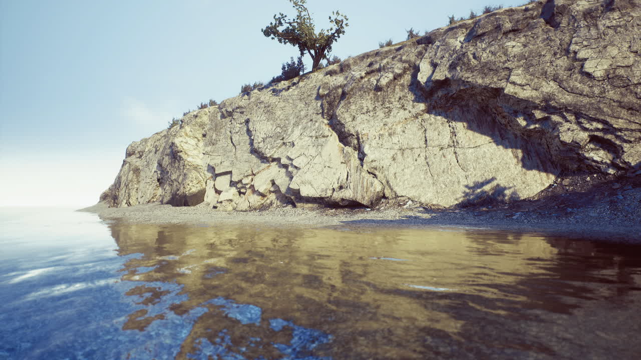 Coastal rock formation with calm water and distant greenery in sunlight