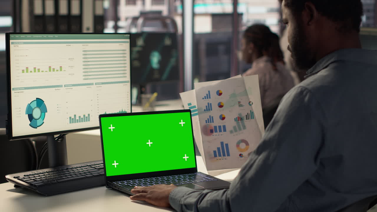 Businessman working on laptop with multiple monitors showing charts and graphs