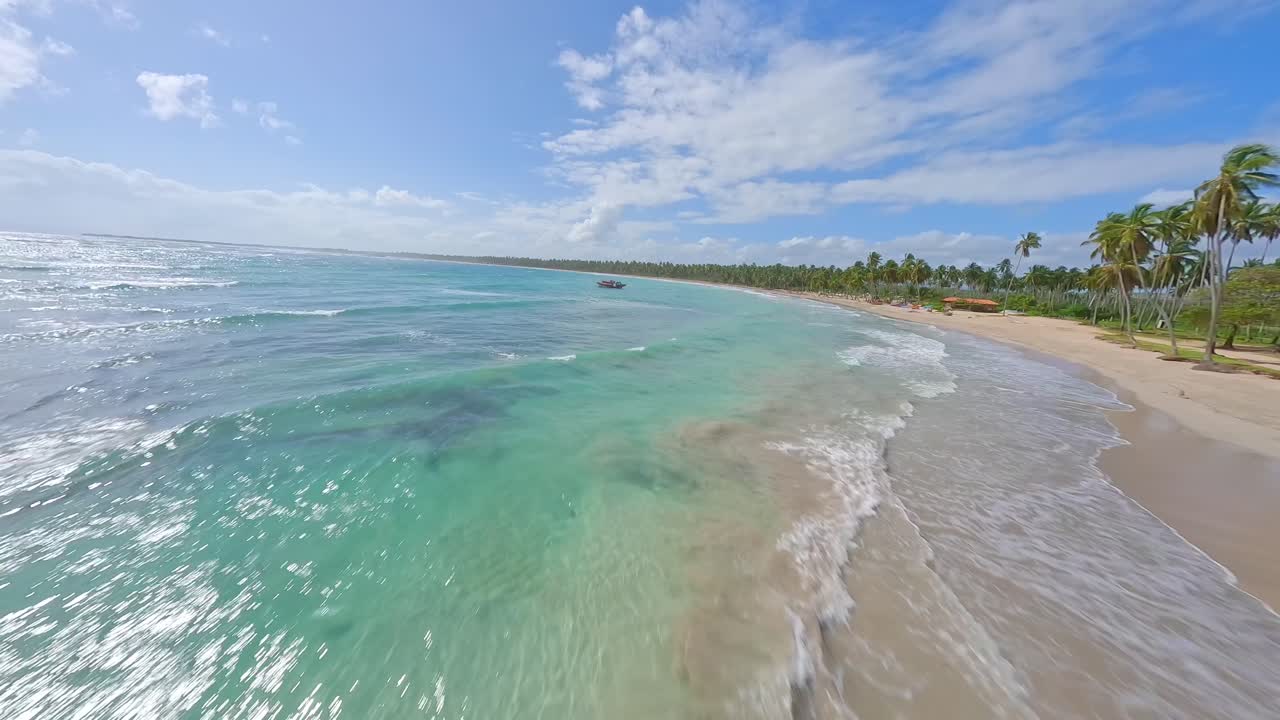 fpv drone disparó sobre la costa del mar caribe con gente jugando y bote anclado - playa los coquitos, república dominicana