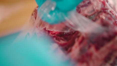 Close-up-view-of-a-man-cutting-the-steak-packed-polythene-wrap-with-a-pair-of-scissors