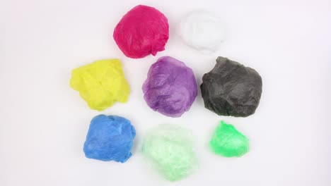 se arrugó en una bola bolsas de plástico usadas de diferentes colores gira sobre fondo blanco, vista de arriba, primer plano, video en bucle, animación en stopmotion, problema ecológico