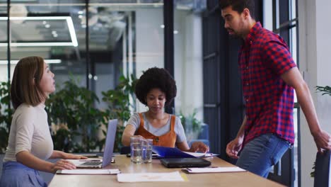 Diverse-business-people-sitting-using-laptop-going-through-paperwork-in-modern-office