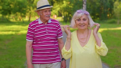 active senior grandfather pensioner walking to stylish grandmother and making a kiss in summer park