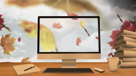 computadora de escritorio y equipos de oficina en una mesa contra las hojas de arce de otoño flotando en el cielo azul
