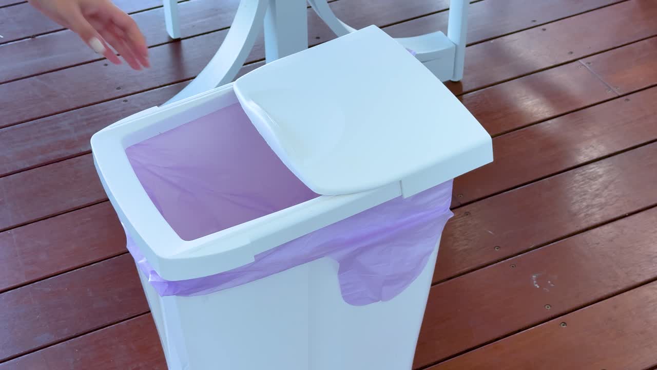 A person places a plastic bottle into a trash bin on a wooden deck, emphasizing responsible waste disposal