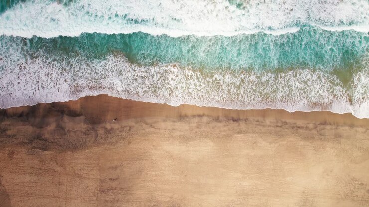 Aerial view of waves crashing on the golden sands of Cofete Beach, Fuerteventura, with vibrant turquoise waters and untouched shoreline.
