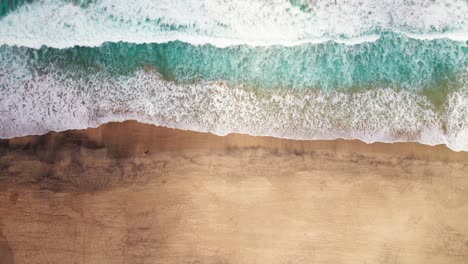 aerial view of waves crashing on the golden sands of cofete beach, fuerteventura, with vibrant turquoise waters and untouched shoreline.