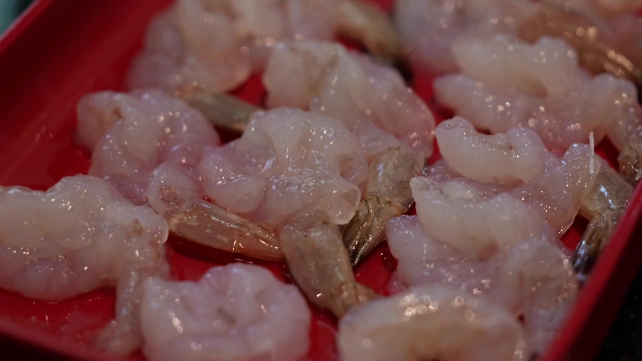 Primo piano di gamberi freschi sgusciati disposti ordinatamente su un piatto, preparati come ingrediente di mare per la cottura shabu shabu e hot pot