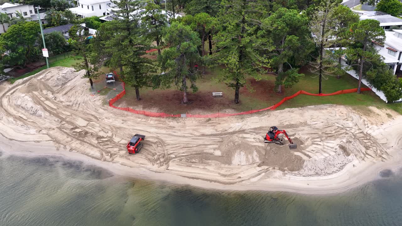 Ripresa aerea con drone di macchinari pesanti che spostano sabbia durante un progetto di ripristino della spiaggia di una proprietà sul lungomare.