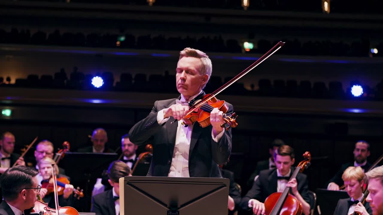 Video captures a dynamic low-angle shot of a violinist in a formal orchestra setting