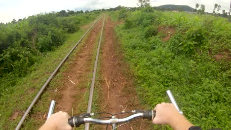 a point of view action shot looking down at a white mans hands on a handle bar while riding a bike along a path next to a railway in africa