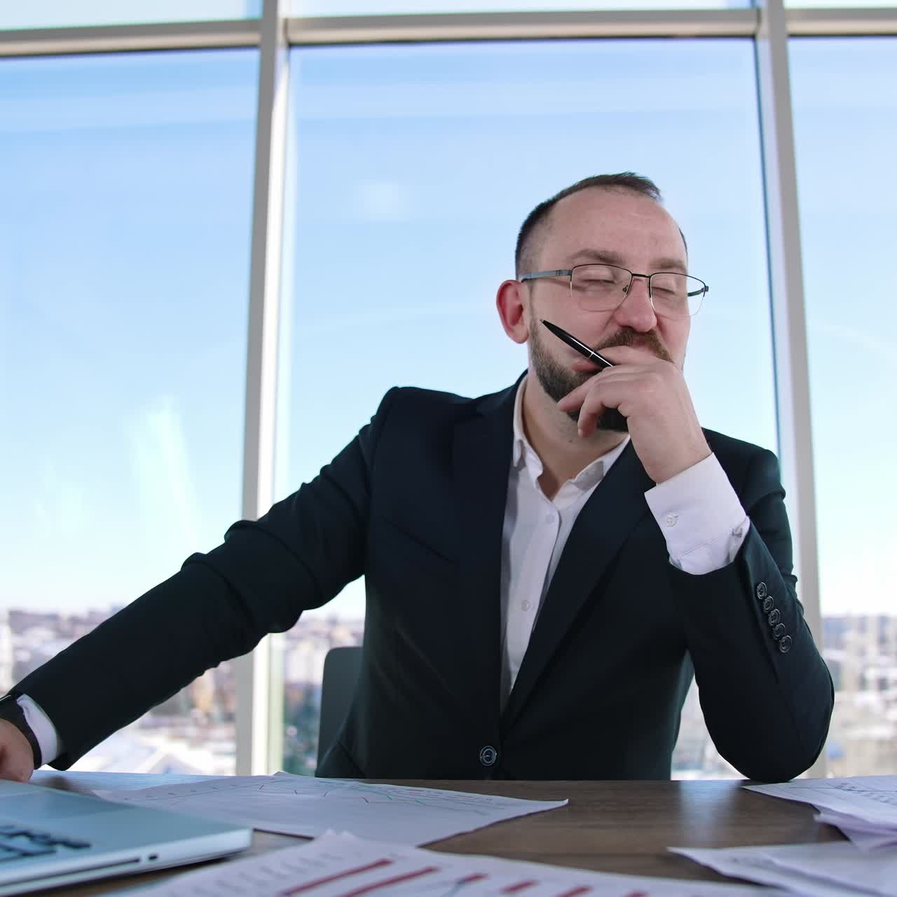 Portrait of a bearded businessman at workplace. Entrepreneur in glasses sitting at desk and thinking about his business