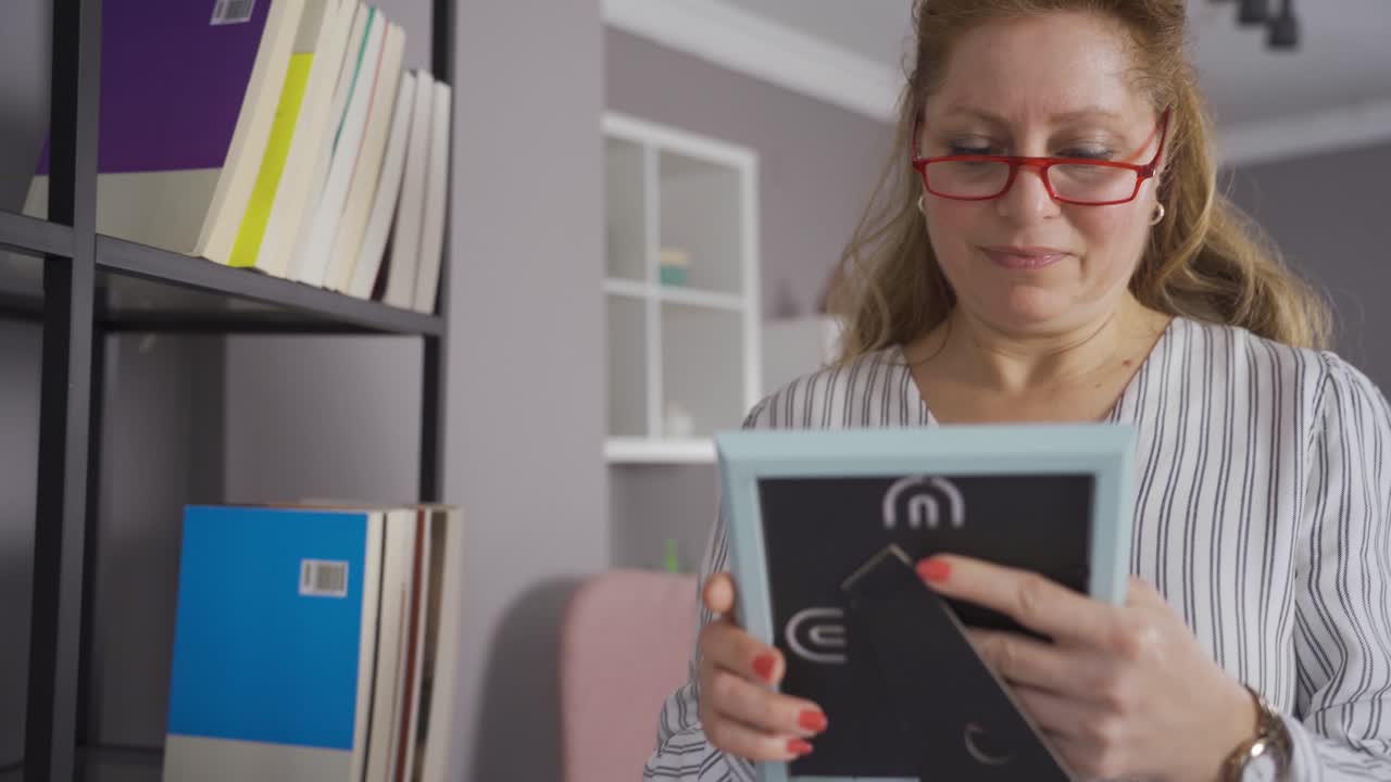 зрелая женщина, живущая одна, смотрит на фотографии своих детей дома и тоскует.