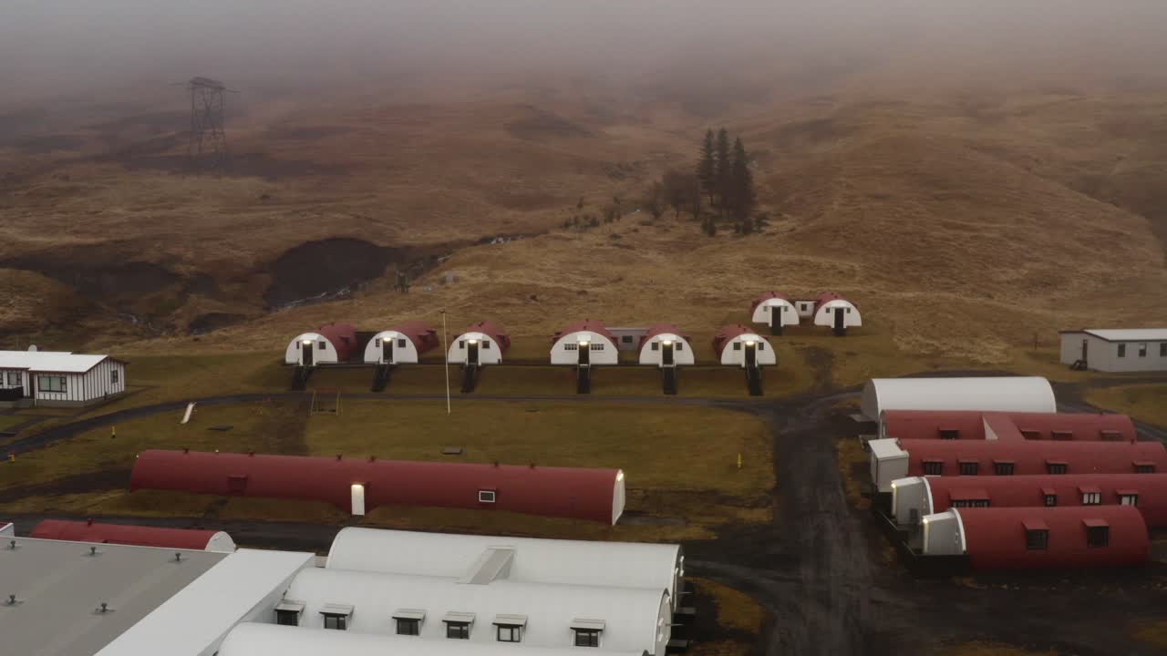 Dronebillede af Quonset-hytter på et græsklædt område i Hvalfjörður, Island, under tåge fra 2. verdenskrig