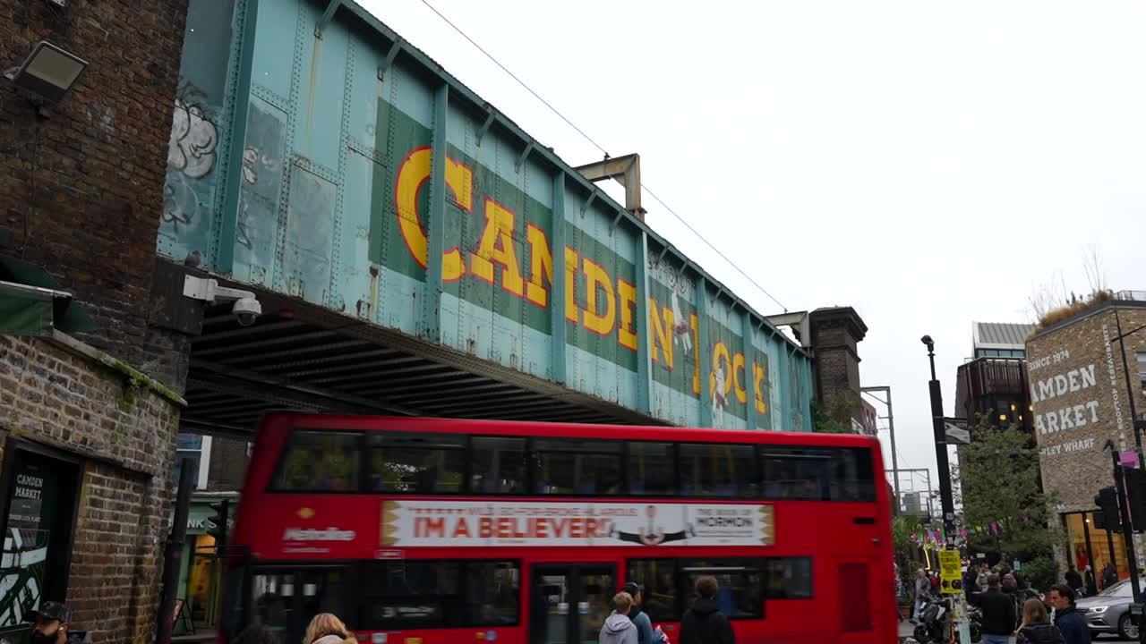 Camden Lock bridge in London with red bus passing beneath and tourists exploring the market nearby