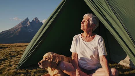 senior woman and dog relaxing in a mountain tent at sunset