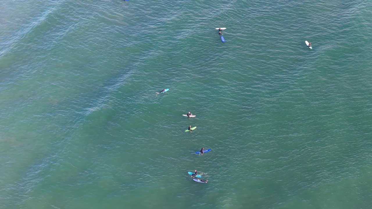 Group of surfers in wetsuits training on surfboards, calm ocean, overhead drone shot, natural daylight