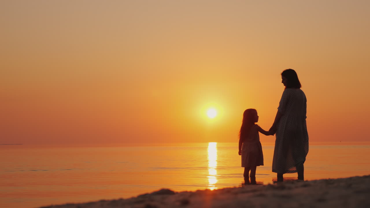 silueta de una mujer embarazada con un bebé cerca de pie cerca del mar al atardecer esperando el seco