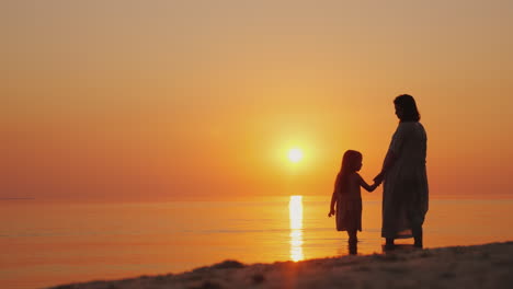 silhouette of a pregnant woman with a baby near by stand near the sea at sunset waiting for the seco