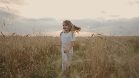 Slow-motion-a-little-girl-of-4-5-years-old-runs-in-a-field-at-sunset-looking-at-the-camera-happy-and-free.-Happy-childhood.-Girl-Running-In-Field-At-Sunset