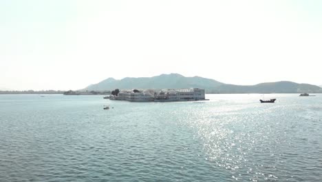 Majestic-white-Taj-Lake-Palace-resting-above-the-surface-of-lake-Pichola-in-Udaipur,-Rajasthan,-India---Aerial-Fly-over-shot