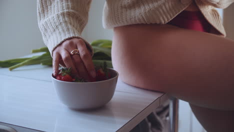 a girl sitted on a table takes strawberries from a basket fruit