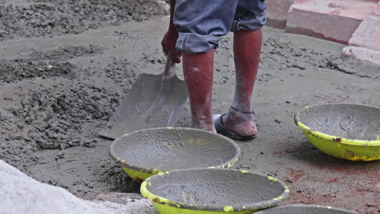 construction worker scooping wet concrete in ghamela at a building site. day time, close up shot, stable shot, 4k