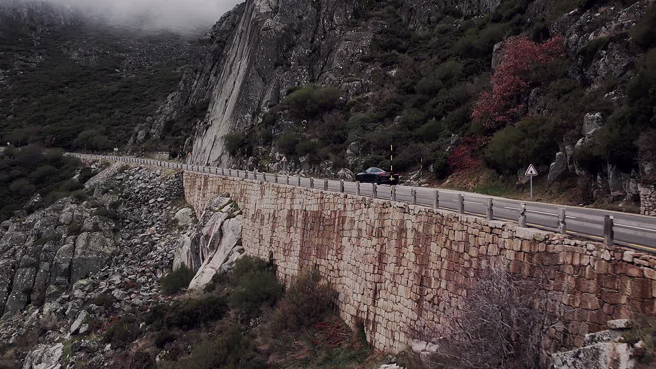 Bil kører på den naturskønne bjergvej N338 i Serra da Estrela, Portugal, mod en baggrund af stenede skråninger og dramatiske klipper, hvilket viser rejser og udforskning, med hurtig indzoomning med drone.