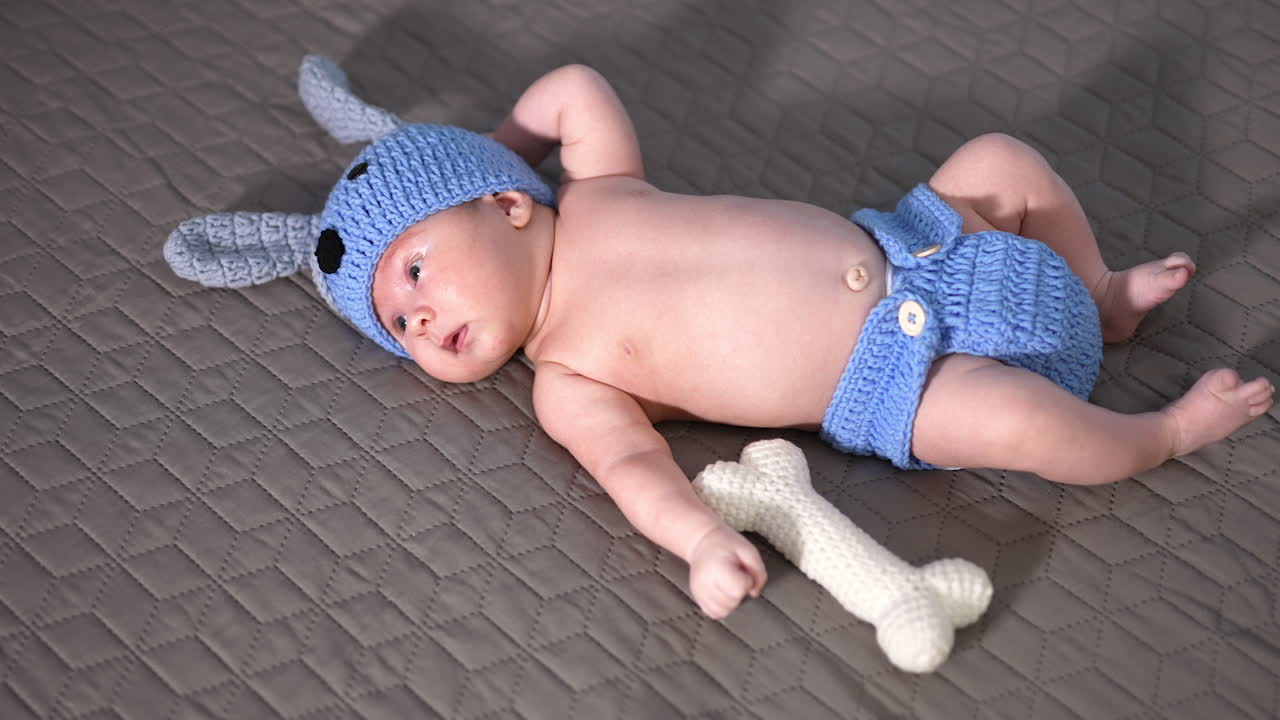 Beautiful little boy in knitted blue costume. Baby boy in puppy suit lying on the grey background. View from above.