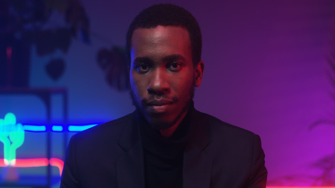 крупный план молодого красивого мужчины, смотрящего в камеру в комнате с неоновыми розовыми и голубыми огнями