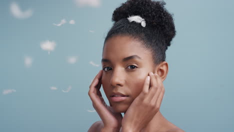 slow motion portrait beautiful african american woman feathers falling on smooth skin touching bare shoulders enjoying natural skincare beauty gently caressing body in blue background