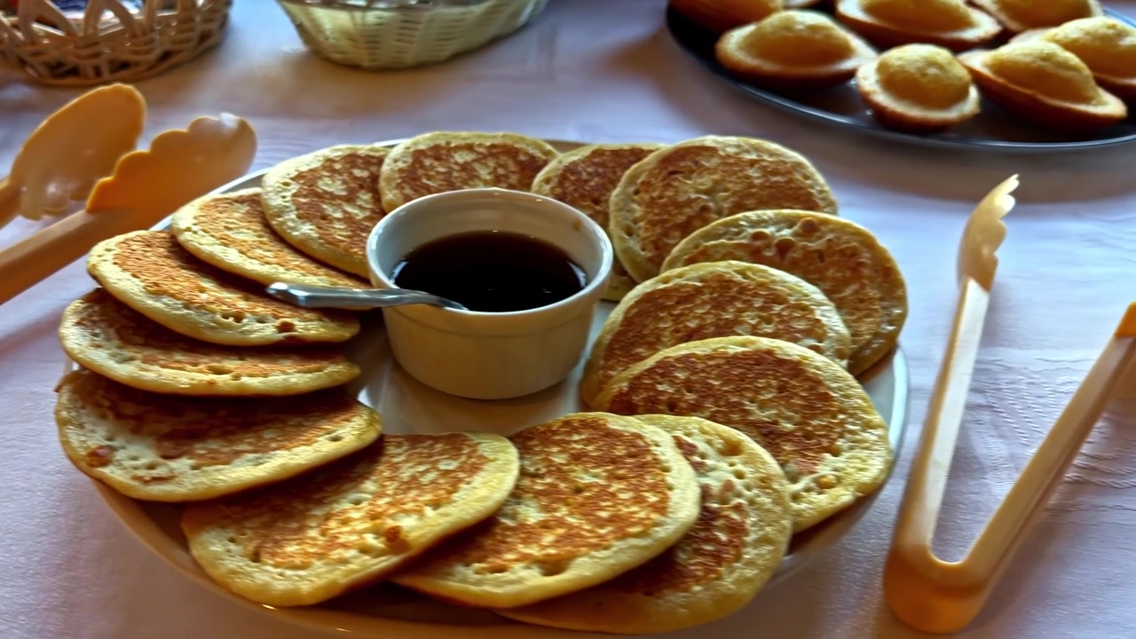 Uma variedade de itens de café da manhã, incluindo pão fresco, panquecas e muffins, são expostos em uma mesa de buffet. Ideal para blogs de culinária ou conteúdo relacionado a alimentos