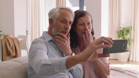 Feliz-Pareja-De-Mediana-Edad-Usando-Un-Teléfono-Inteligente-Teniendo-Video-Chat-Saludando-A-Sus-Nietos-Disfrutando-De-Una-Comunicación-En-Línea-Relajante-Casa-De-Retiro