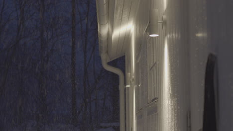 snowfall at night near glowing building exterior, static view