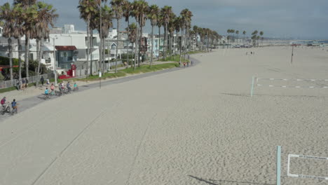 Antena:-Vuelo-Sobre-La-Playa-Con-Redes-De-Voleibol-En-Venice-Beach-Con-Palmeras-Y-Carril-Bici,-Soleado,-Los-Angeles-California