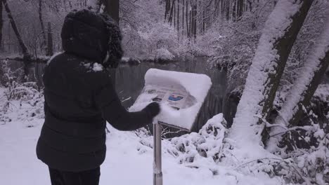 warm dressed female removing snowfall from information board overlooking niebieskie zrodla woodland river