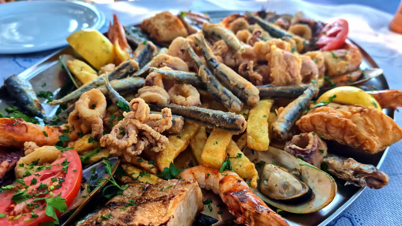 Seafood and fried fish platter on a table next to the Mediterranean Sea. Zoom out