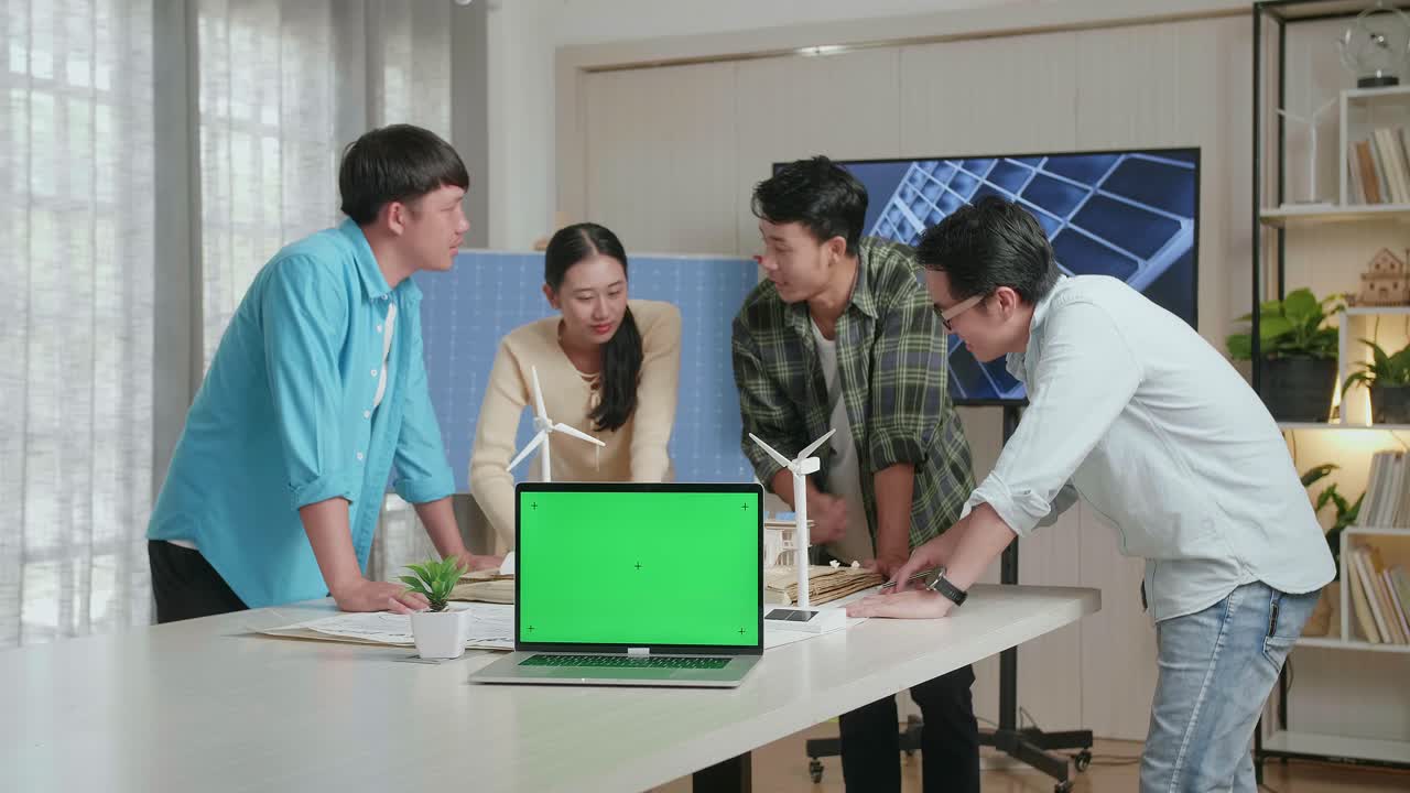 아시아 엔지니어 그룹이 사무실에서 태양 전지판을 가진 작은 집 모델에 대해 논의하는 동안 테이블에 녹색 화면 노트북