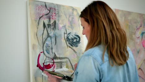 Female-artist-painting-figure-on-a-canvas,-stood-in-a-home-studio