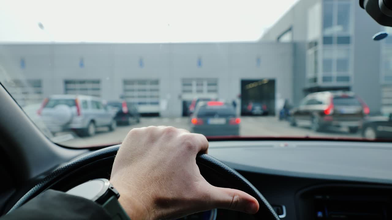 Cars queue in front of inspection hall as man waits calmly behind the wheel