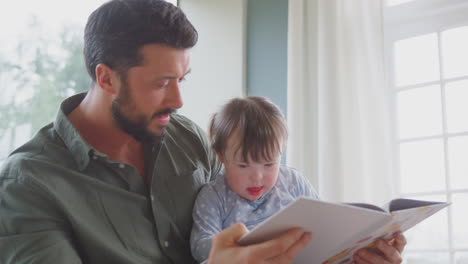 Padre-Con-Hija-Con-Síndrome-De-Down-Leyendo-Un-Libro-Juntos-En-Casa