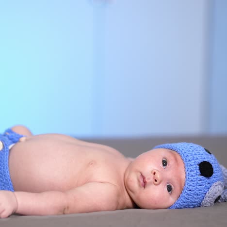 toddler in a cute knitted cap with ears and diaper lying on the bed. sweet child looking attentively at the camera. side view