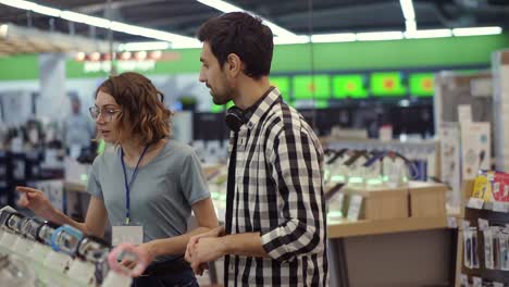 pretty female consultant gives professional advice to a young man. he considers to buy a new smart watches and needs expert opinion. store is modern, bright and has all the new devices. slow motion