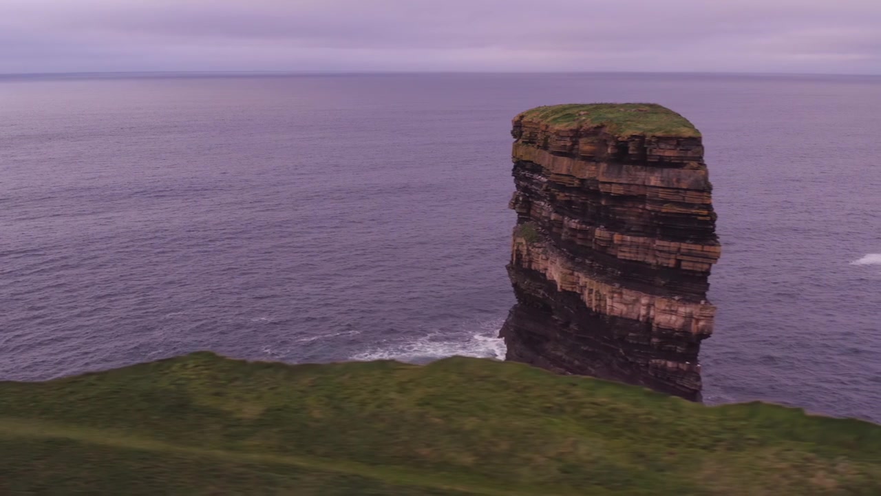 Aerial tracking right along grassy cliffs with the rugged Dun Briste sea stack at Downpatrick Head Ireland
