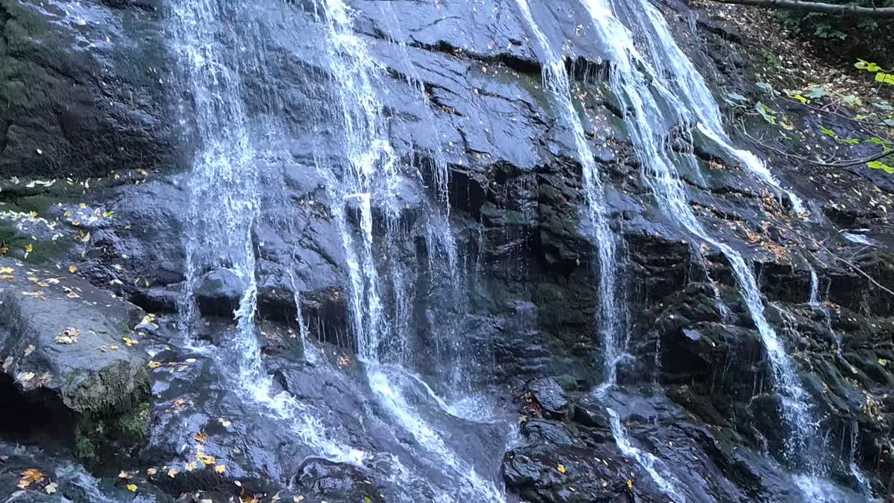 Strong waterfall streaming over dark rocks with white water motion in forest setting