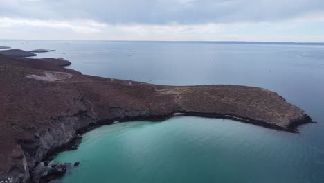 Aerial-shot-of-Playa-Balandra's-clear-turquoise-waters-and-rugged-coastline-at-dusk